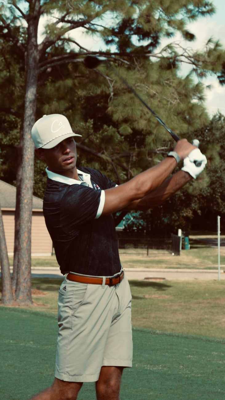 Golfer in a Capstone Golf polo and rope hat following through on a swing